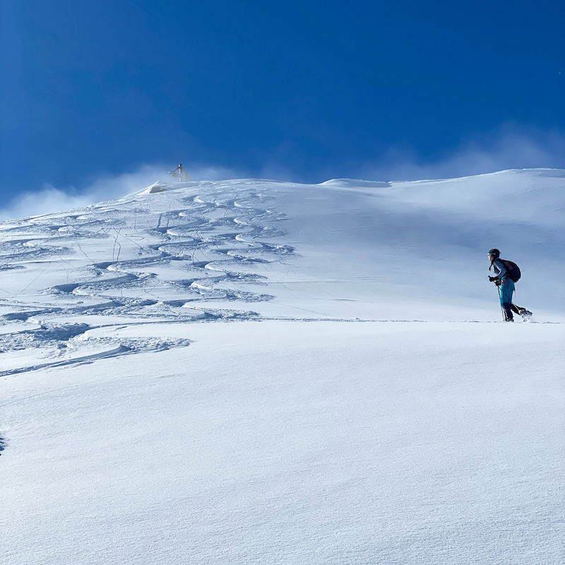 Skitouring with kids. Girl at 12 walks up to a summit with a cross.